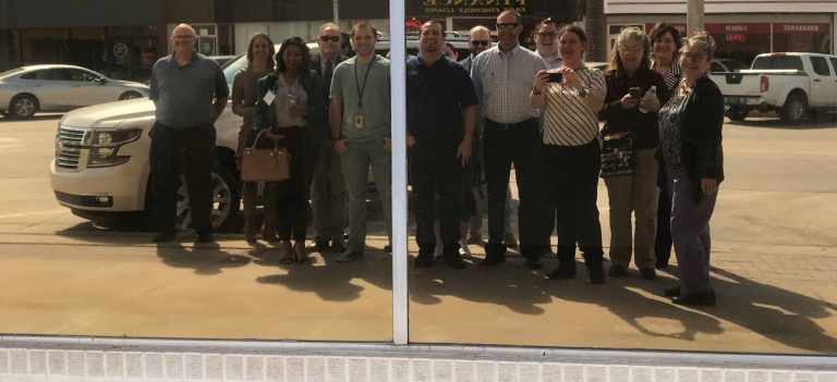 Becky McCray leading a group in a downtown tour of Ada, Oklahoma, paused for a selfie, reflected in a store window.