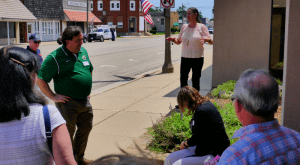 Becky McCray leading a downtown walkthrough, as one person stops to pull weeds from a flower bed.