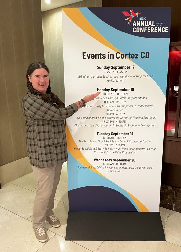 Becky McCray standing next to a stand up banner listing the sessions in a conference track.