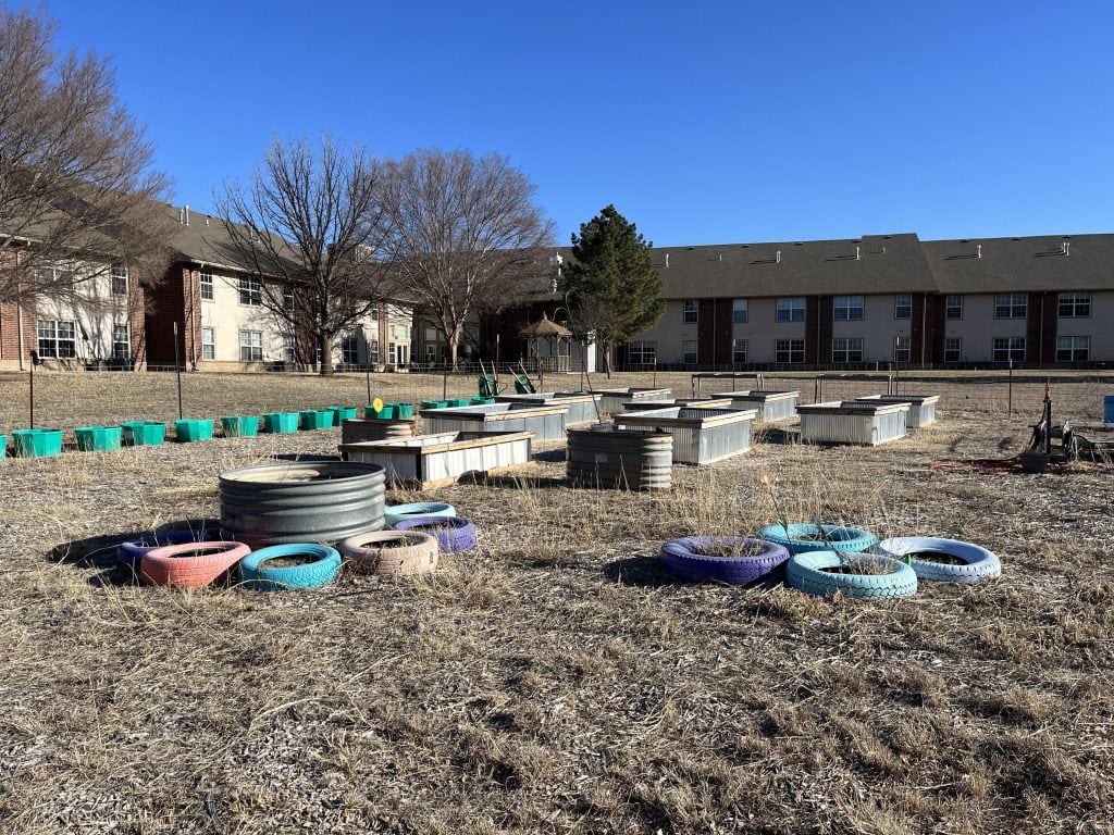 Raised beds, old water tanks and tires converted to make a community garden behind an apartment building. It's late winter, so nothing is growing yet. 