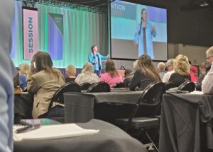 In a large conference room, Becky McCray is on stage and on the big screen with an interested audience