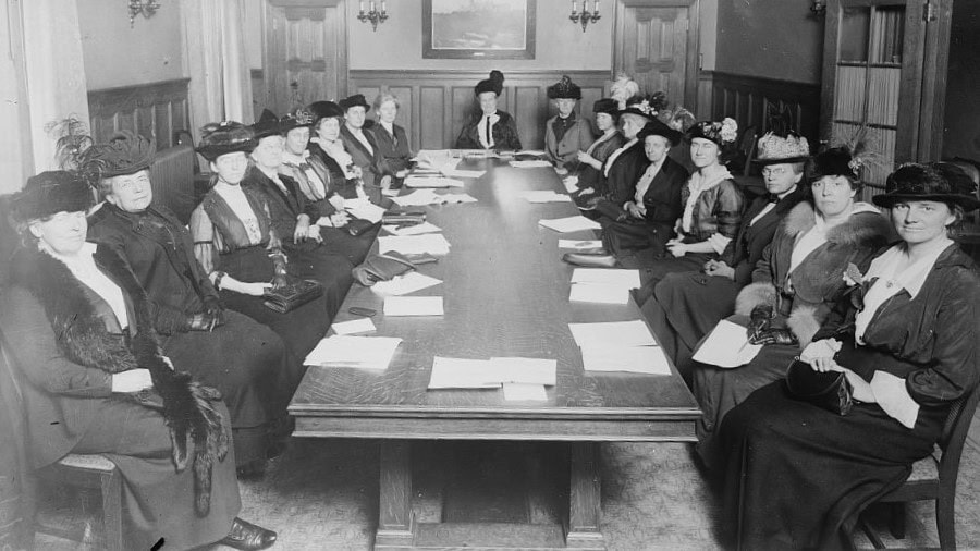 Women seated around a board table conducting a meeting, circa 1910