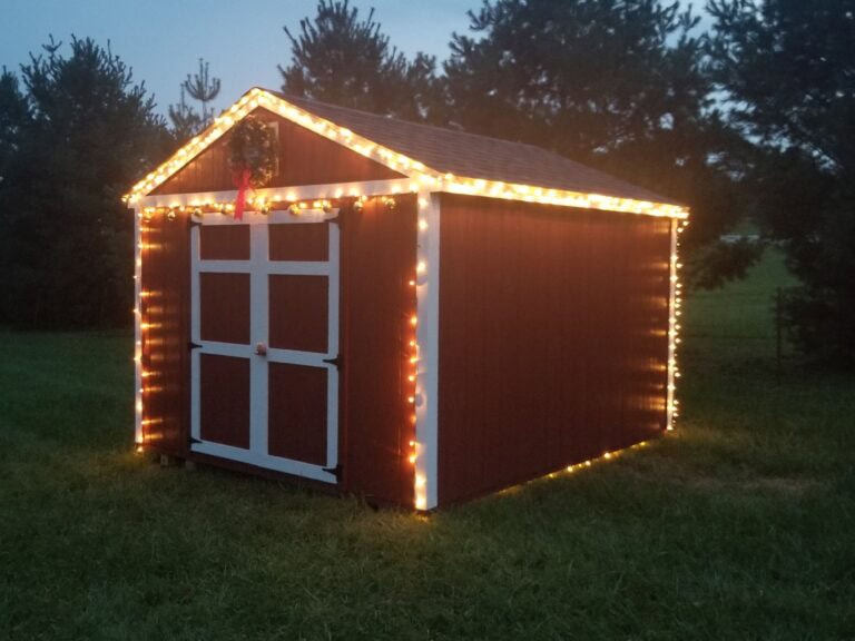 A red storage shed with white trim is decorated with clear holiday light strings