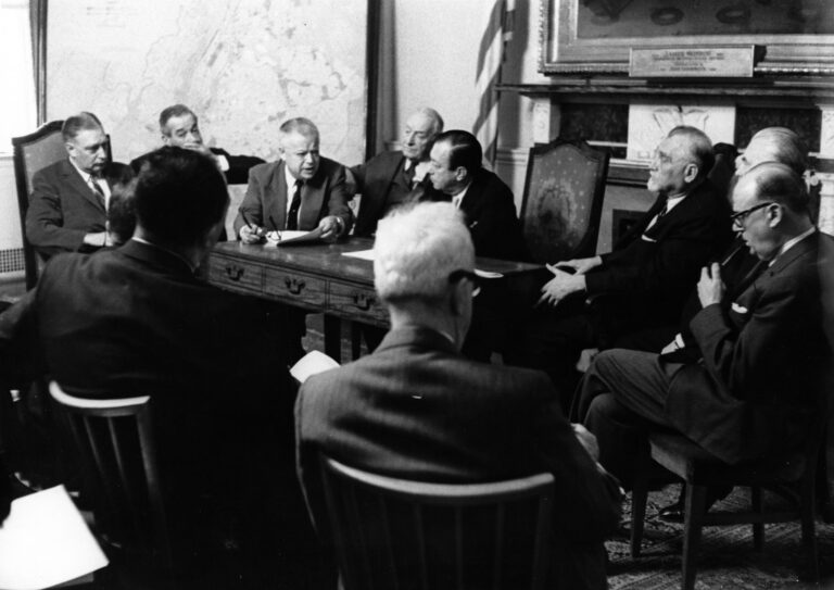 Ten men around a conference table in a 1950s era photo