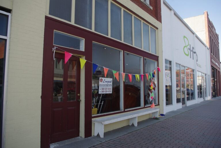 A downtown building with a for sale sign and pennants draped across the front of the windows.