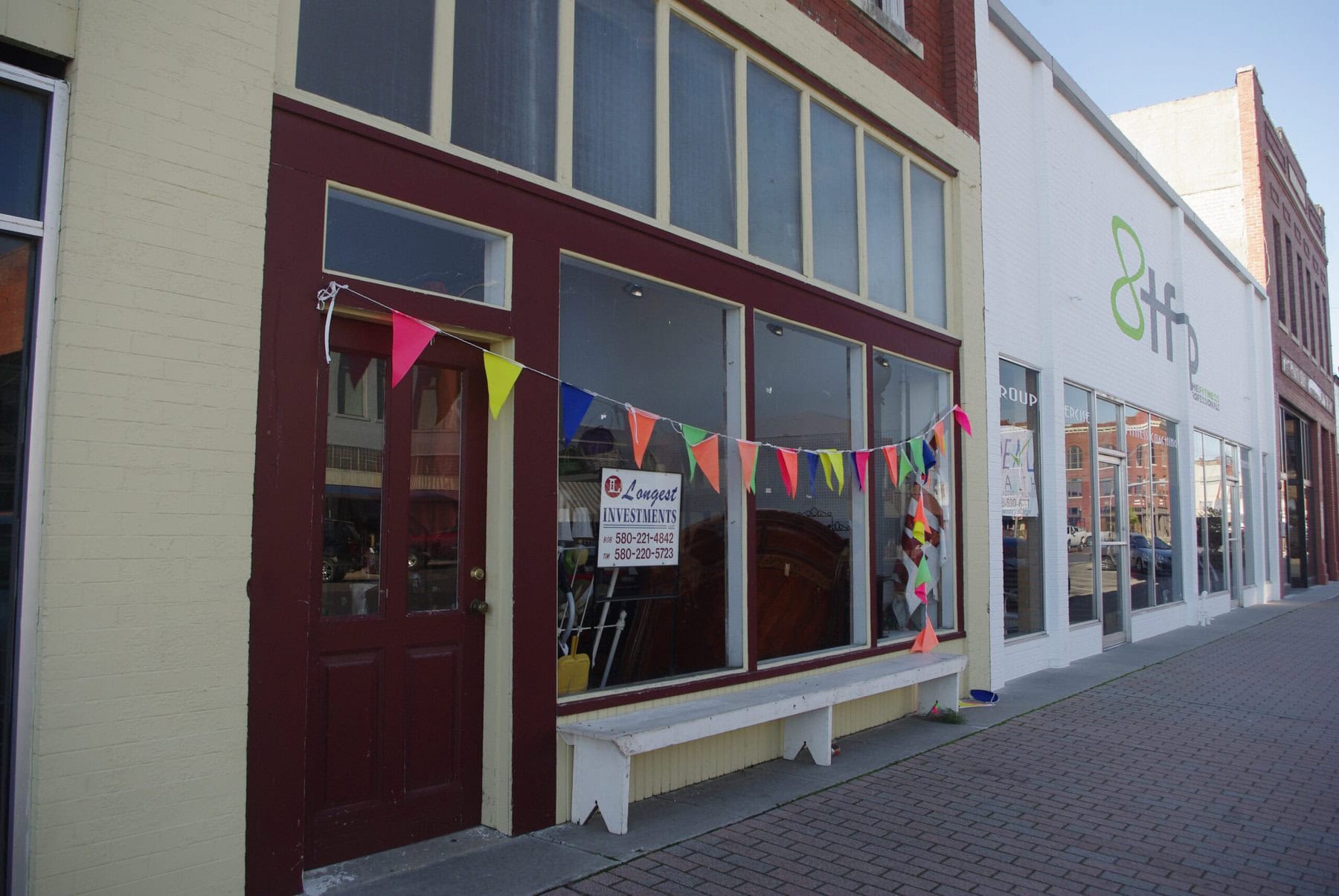 A downtown building with a for sale sign and pennants draped across the front of the windows.