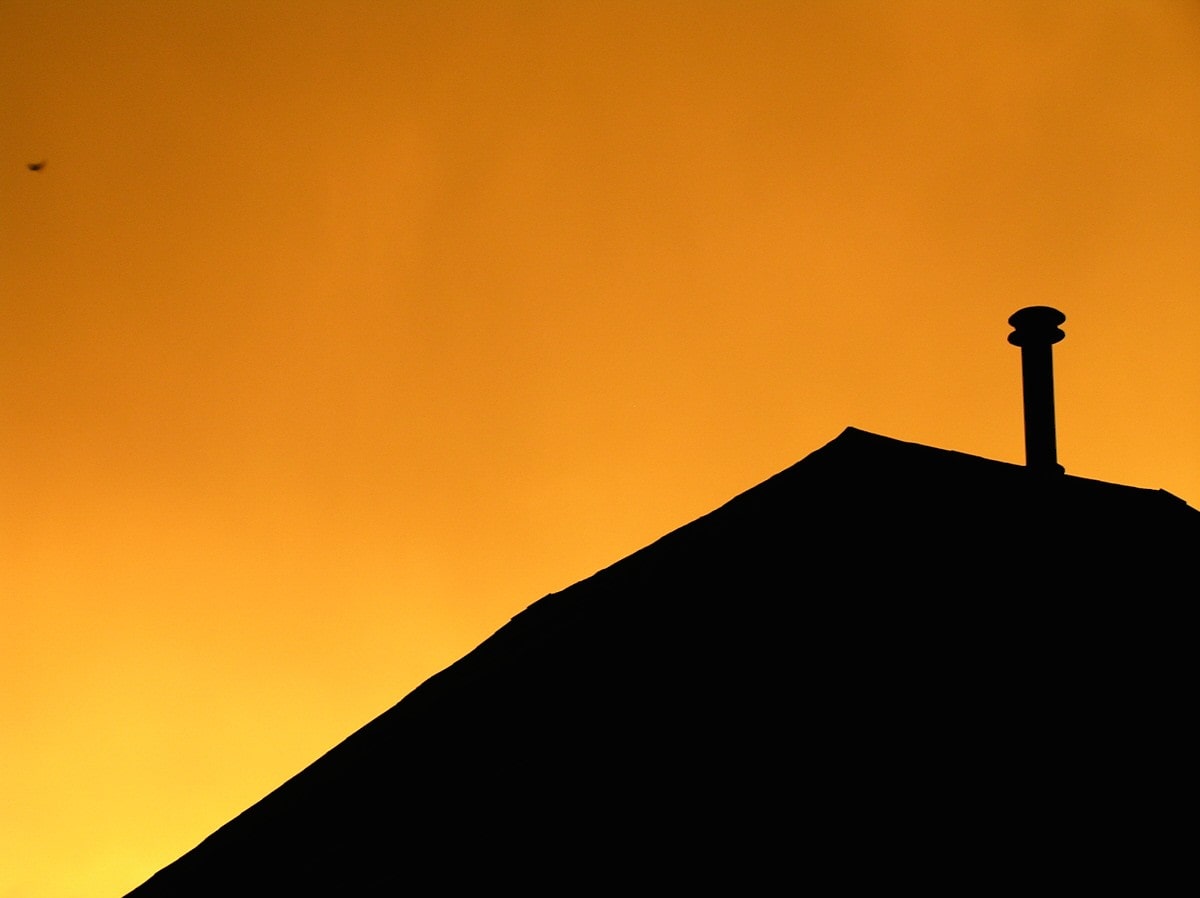 The silhouette of a small rural house against an orange sunset background