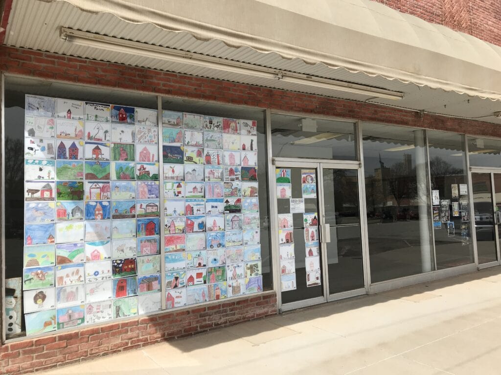 An empty downtown building with dozens of crayon drawings by kids displayed in neat rows inside the windows.