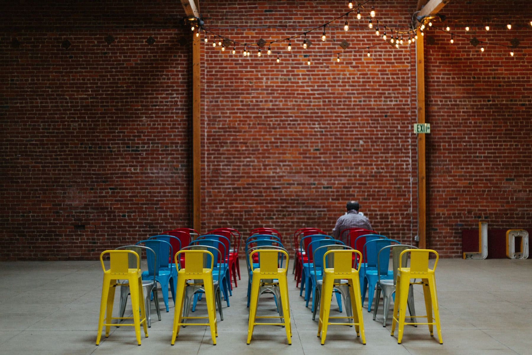rows of colorful chairs are empty, except for one person in the front row facing away from the camera