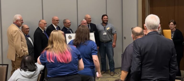 A group of people pose with a ceremonial big check while a person with a manila envelope holds the contracts to sign