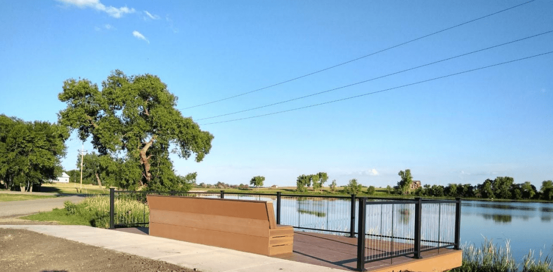 A handicapped accessible deck with a bench and railing offers a view over a shallow pond. Photo courtesy of Town of Milnor, North Dakota.