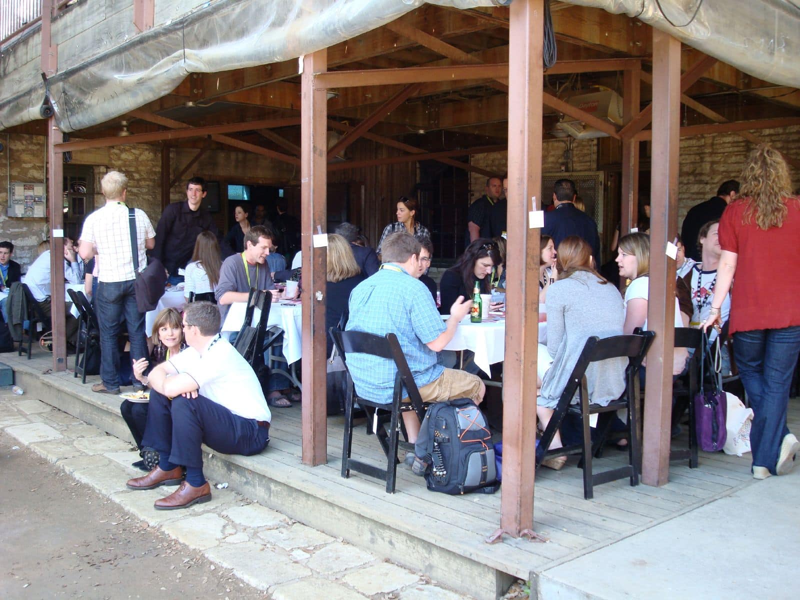 a group of people eating and talking together on a patio. People are sitting in chairs, seated on the step and standing around in conversations.