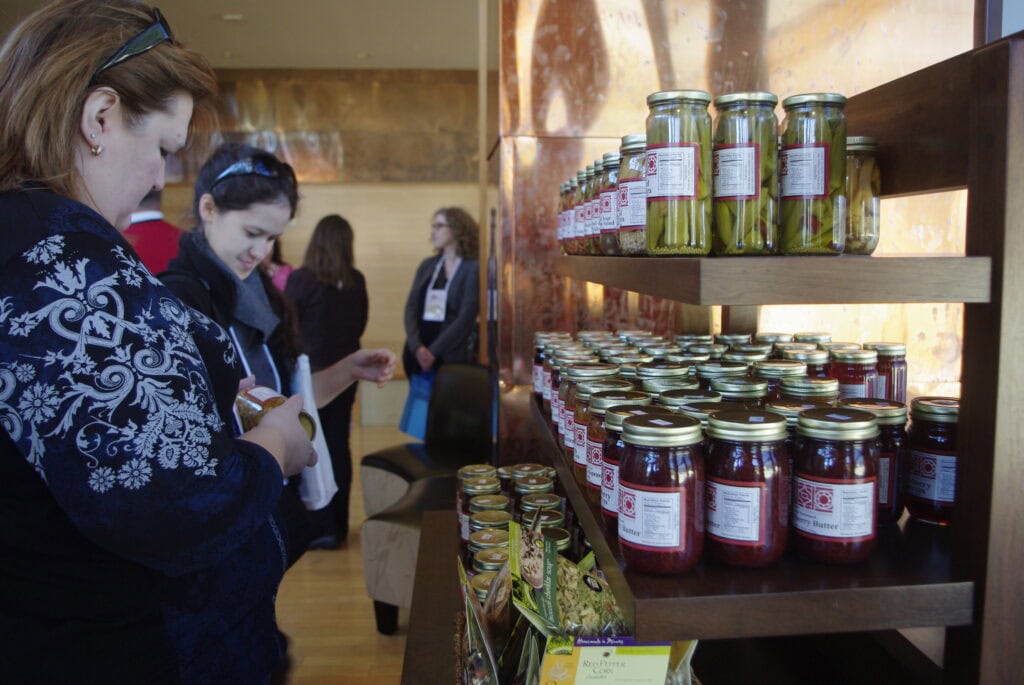 Two women are shopping from a local food products display filled with jars and packages.