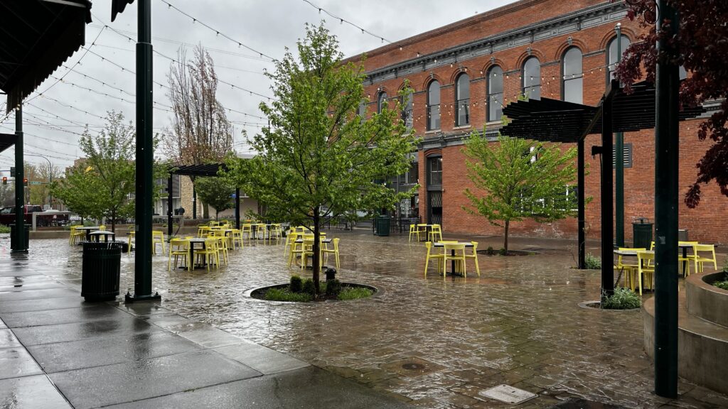 Plaza with yellow tables and chairs on stamped concrete and a pergola with string lights overhead.